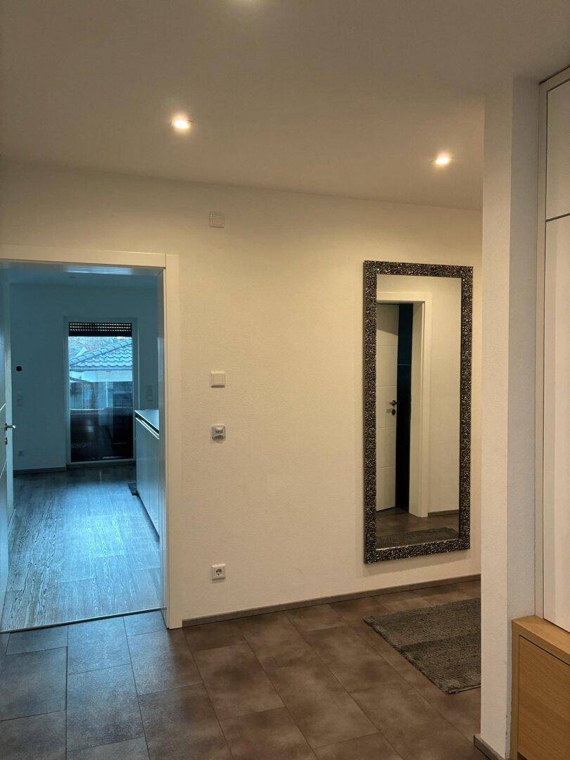 Heller Flur mit Fliesenboden und einem großen, dekorativen Wandspiegel.