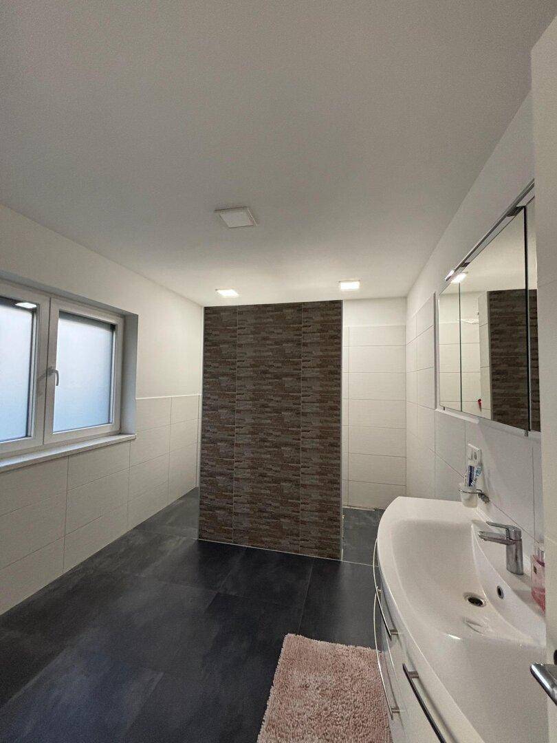 Geräumiges Badezimmer mit modernem Waschbecken, Spiegelschrank und begehbarer Dusche.