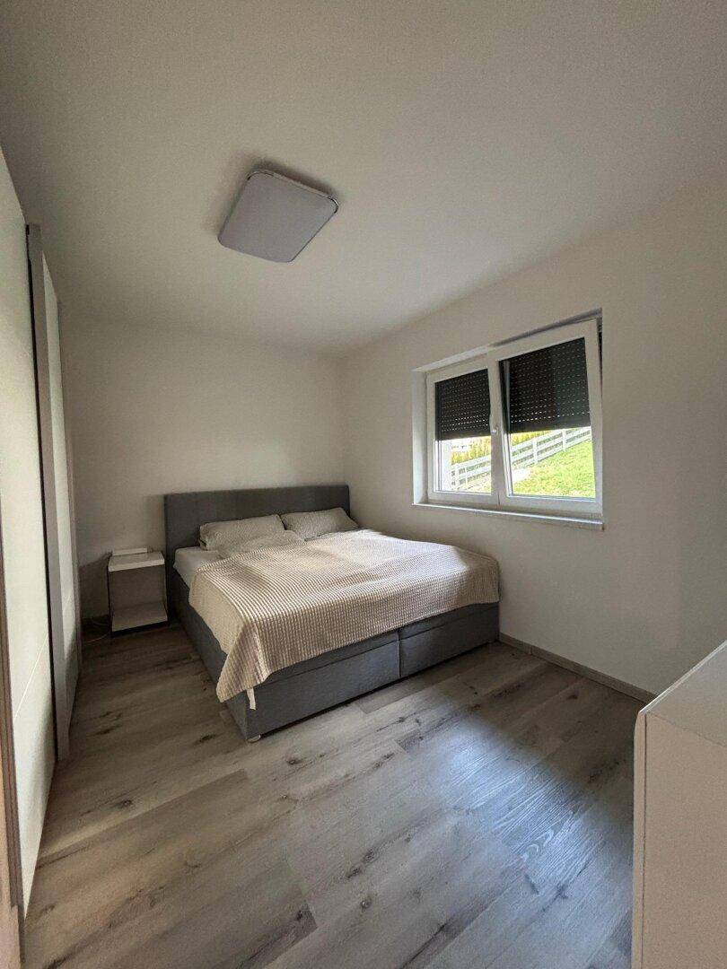Gemütliches Schlafzimmer mit Doppelbett, Nachttisch und Fenster mit Rollladen.