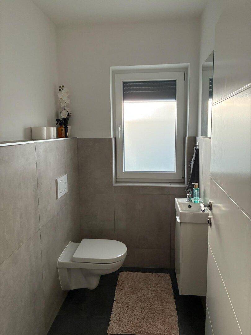 Modernes Gäste-WC mit wandhängender Toilette, kleinem Waschbecken und Fenster.