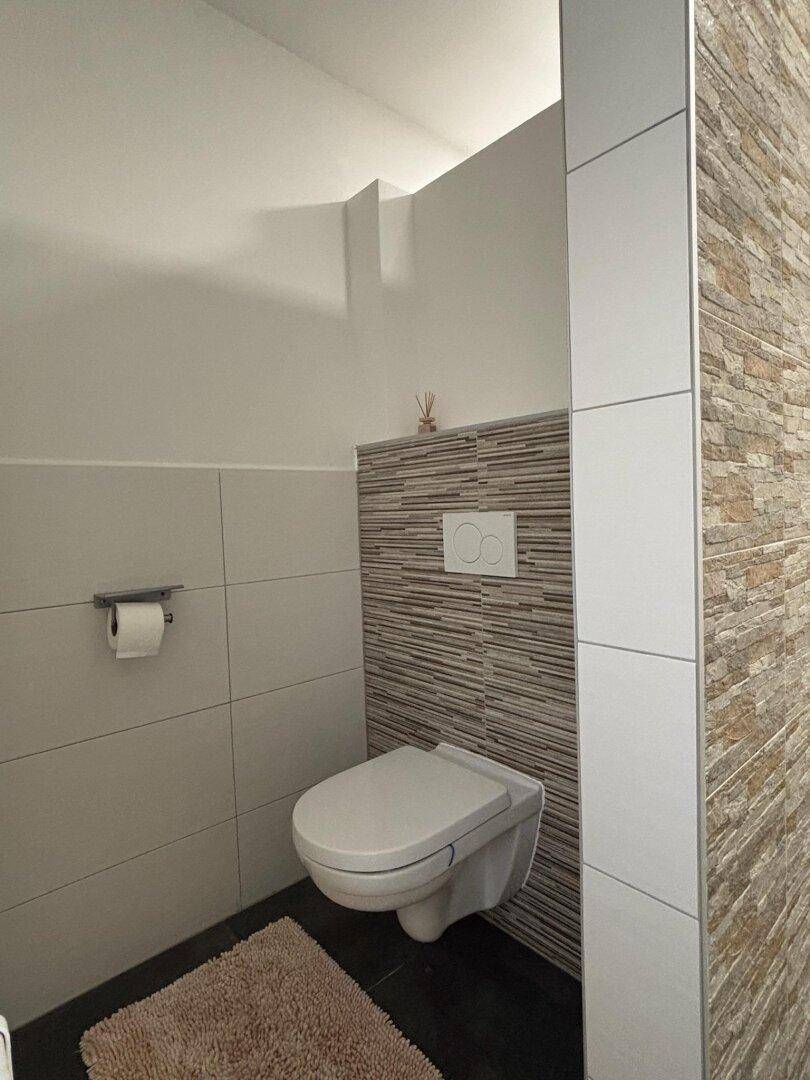 Stilvolles Gäste-WC mit wandhängender Toilette und dekorativer Fliesenwand.