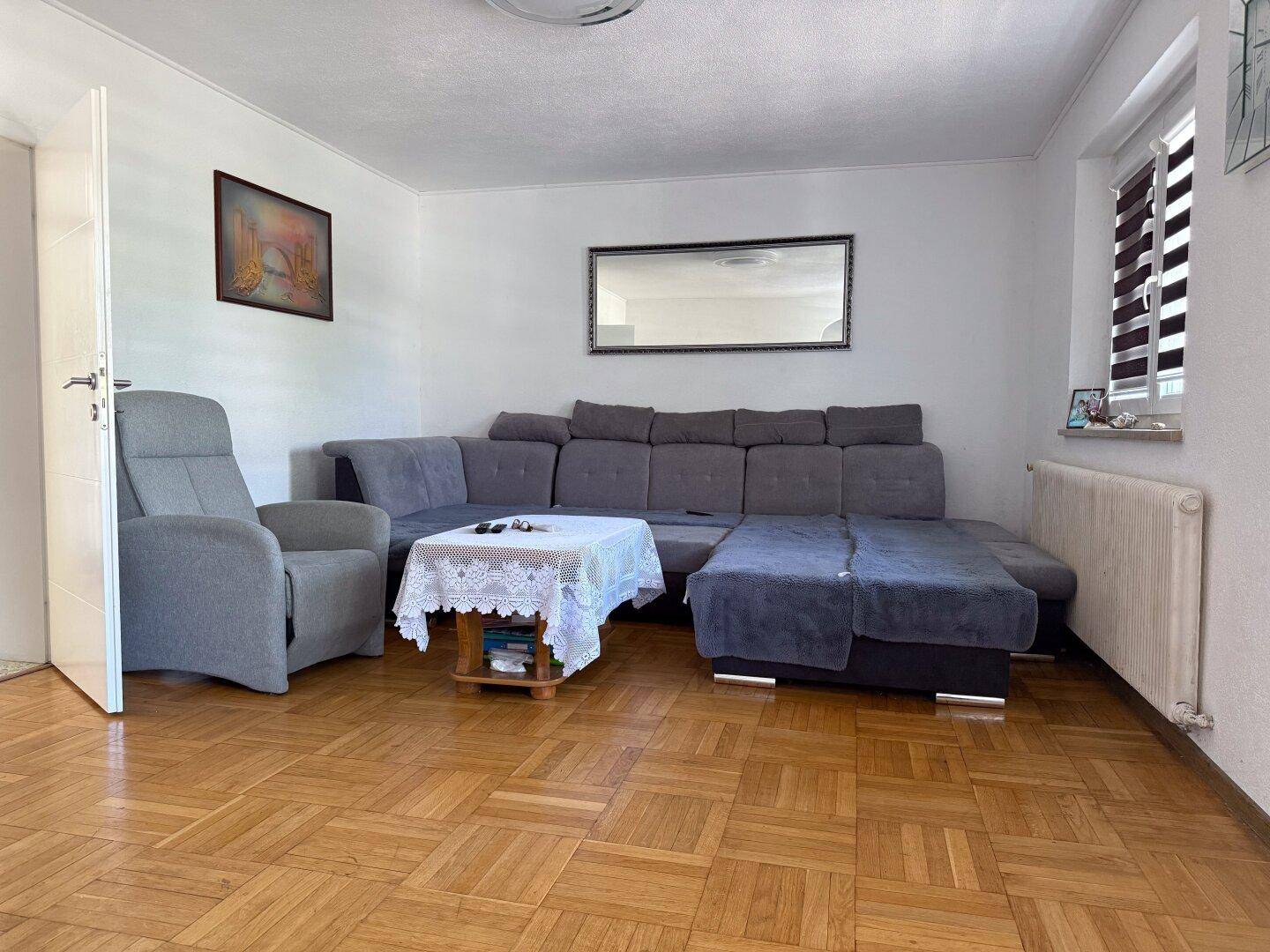 Gemütliches Wohnzimmer mit großem Ecksofa, Sessel und klassischem Parkettboden.