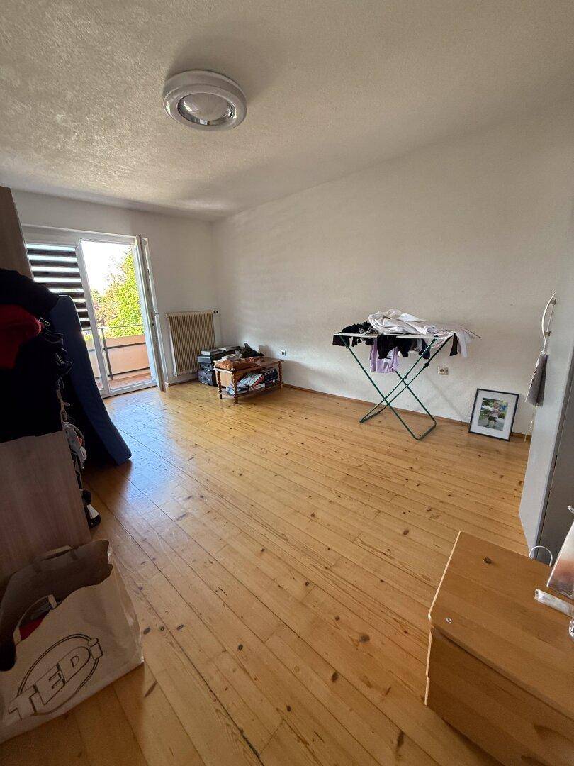 Helles Zimmer mit Holzdielenboden und Zugang zu einem Balkon, ideal als Schlaf- oder Gästezimmer.