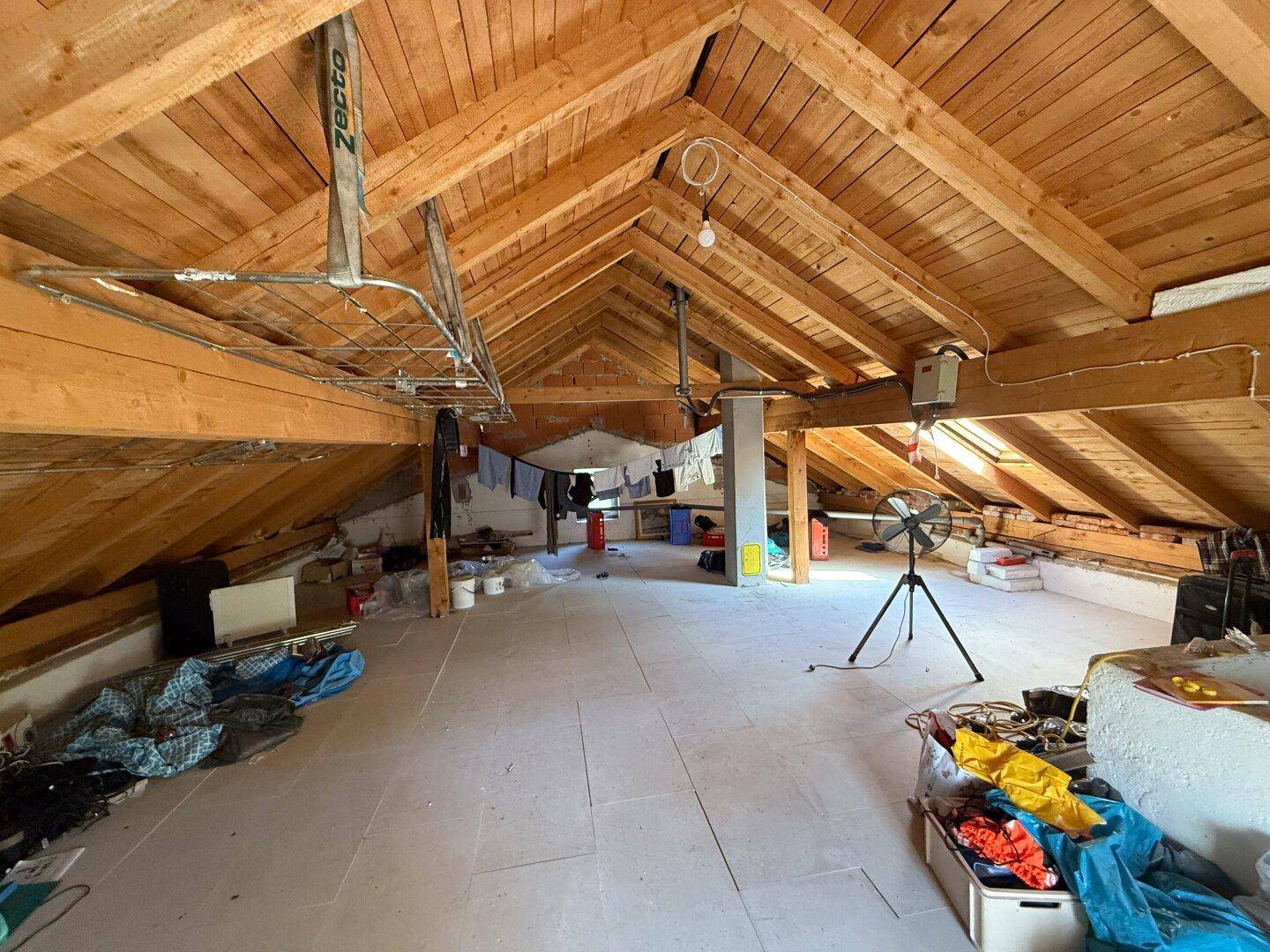 Geräumiger Dachboden mit sichtbaren Holzbalken und Fliesenboden, bietet viel Stauraum.