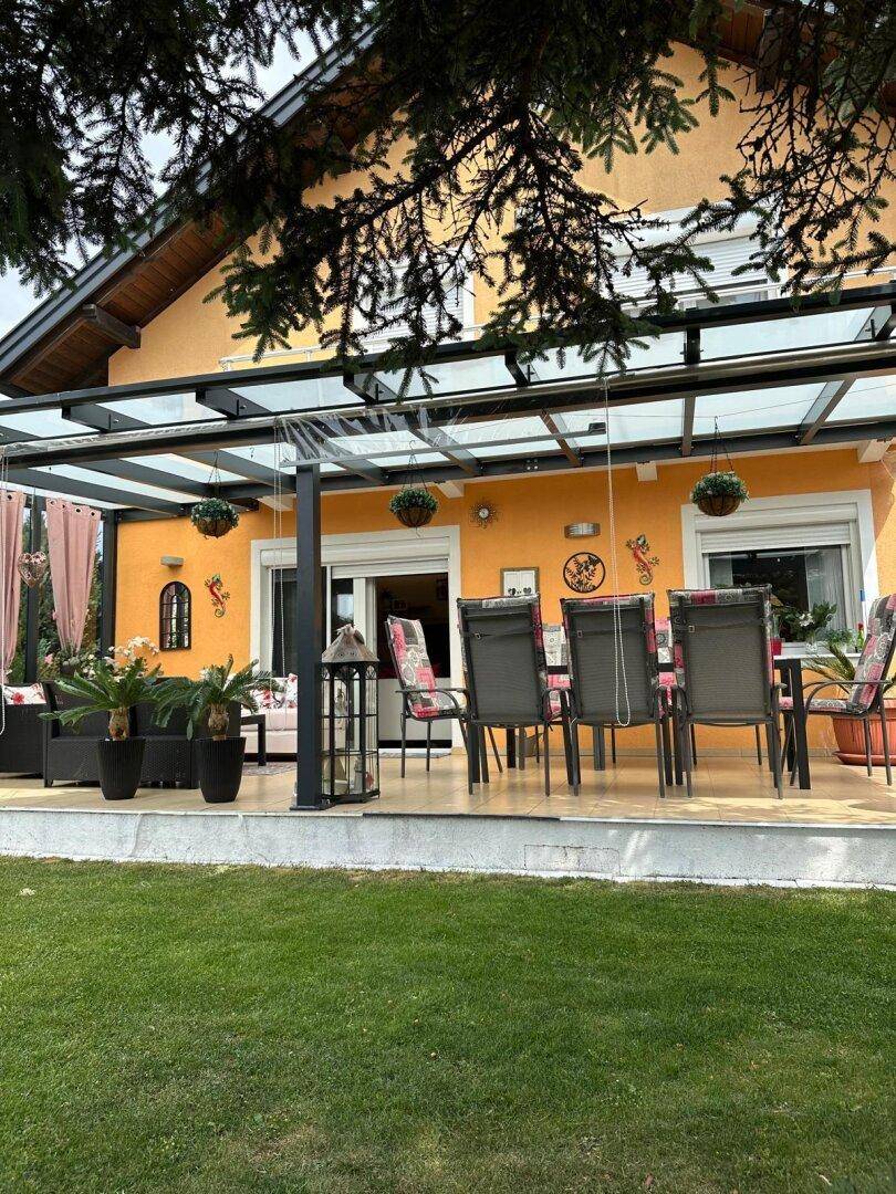 Überdachte Terrasse mit Essbereich und Lounge-Möbeln, umgeben von einem gepflegten Garten.