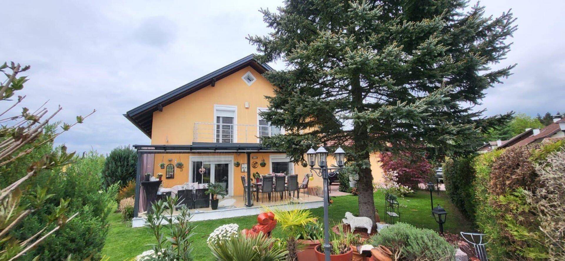 Rückansicht des Hauses mit großer Terrasse, weitläufigem Garten und altem Nadelbaum.