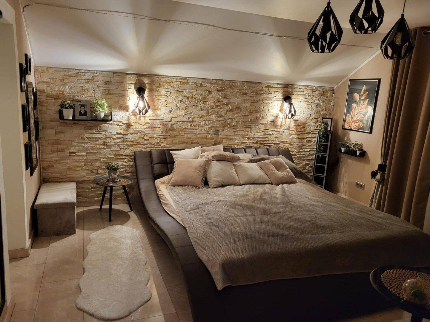 Geräumiges Schlafzimmer mit indirekter Beleuchtung, Steinwand und großem Doppelbett.