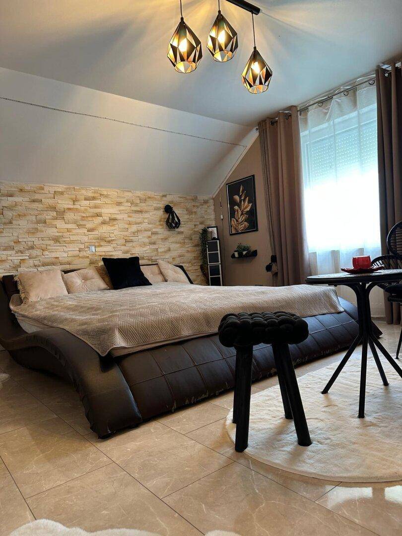 Helles Schlafzimmer mit Dachschräge, Steinwand und modernem Bettgestell.