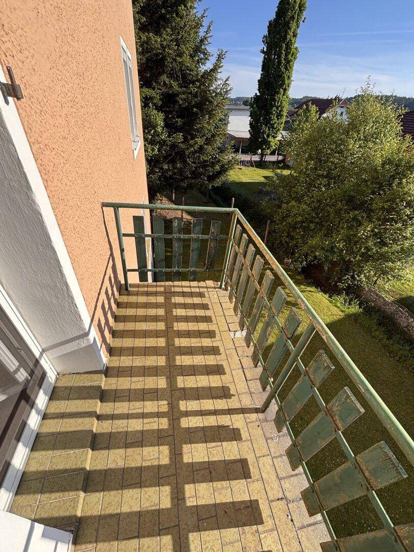 Kleiner Balkon mit grüner Brüstung und sonnigem Blick auf den Gartenbereich.