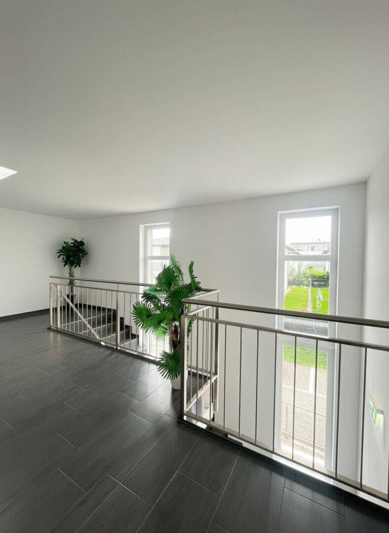 Oberes Treppenhaus mit Blick ins Grüne, dunklen Fliesen und modernen Edelstahlgeländern.