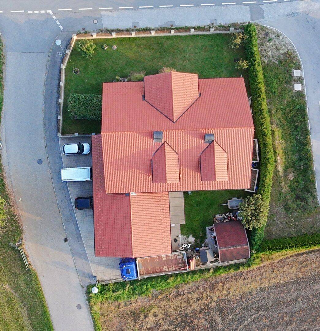 Senkrechte Luftaufnahme des Hauses mit rotem Ziegeldach, umgeben von einem gepflegten Garten und Zufahrt.