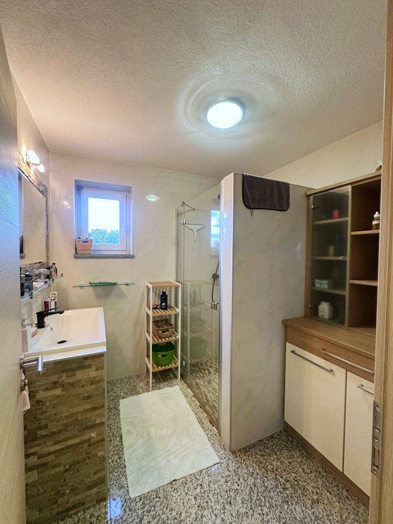 Helles Badezimmer mit moderner Dusche, Einzelwaschbecken und Fenster für Tageslicht.