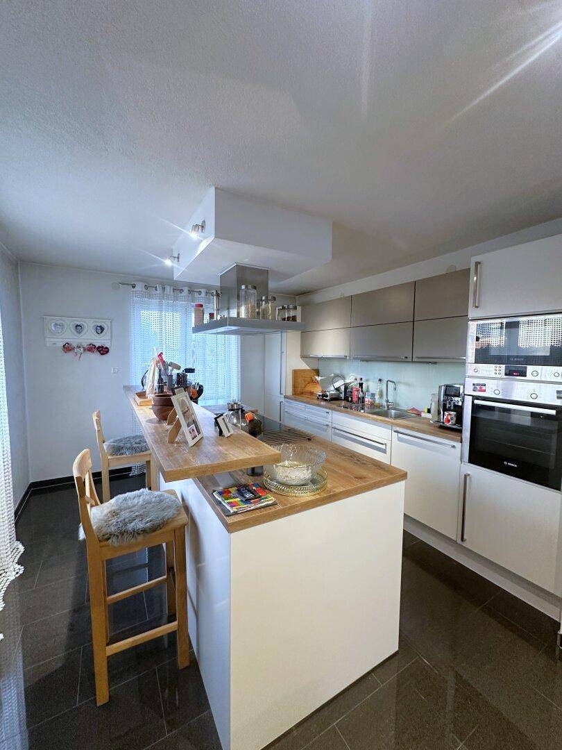 Moderne Küche mit Kochinsel, Holztheke und integrierten Geräten, ideal für geselliges Kochen.
