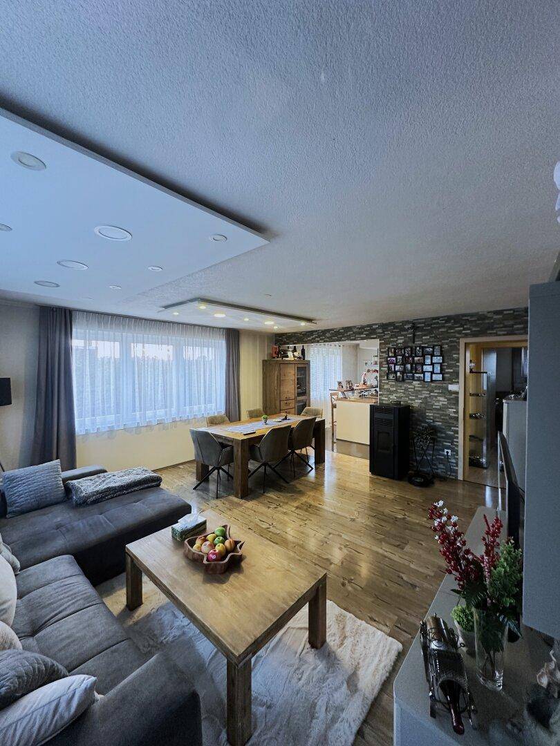Geräumiger Wohnbereich mit großem Sofa, Holzboden und Blick auf den Essbereich und die Küche.