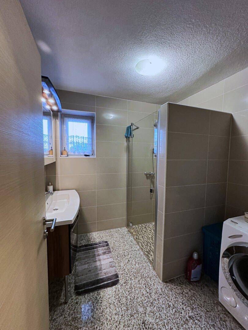 Modernes Badezimmer mit Dusche, Waschbecken und Waschmaschine, hell gefliest und funktional.