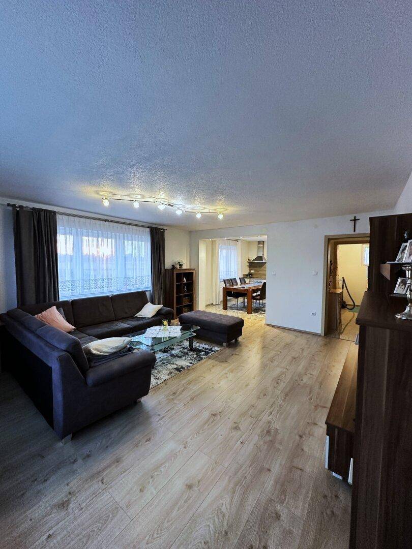 Offener Wohnbereich mit Laminatboden, großem Sofa und Blick auf den Essbereich und die Küche.