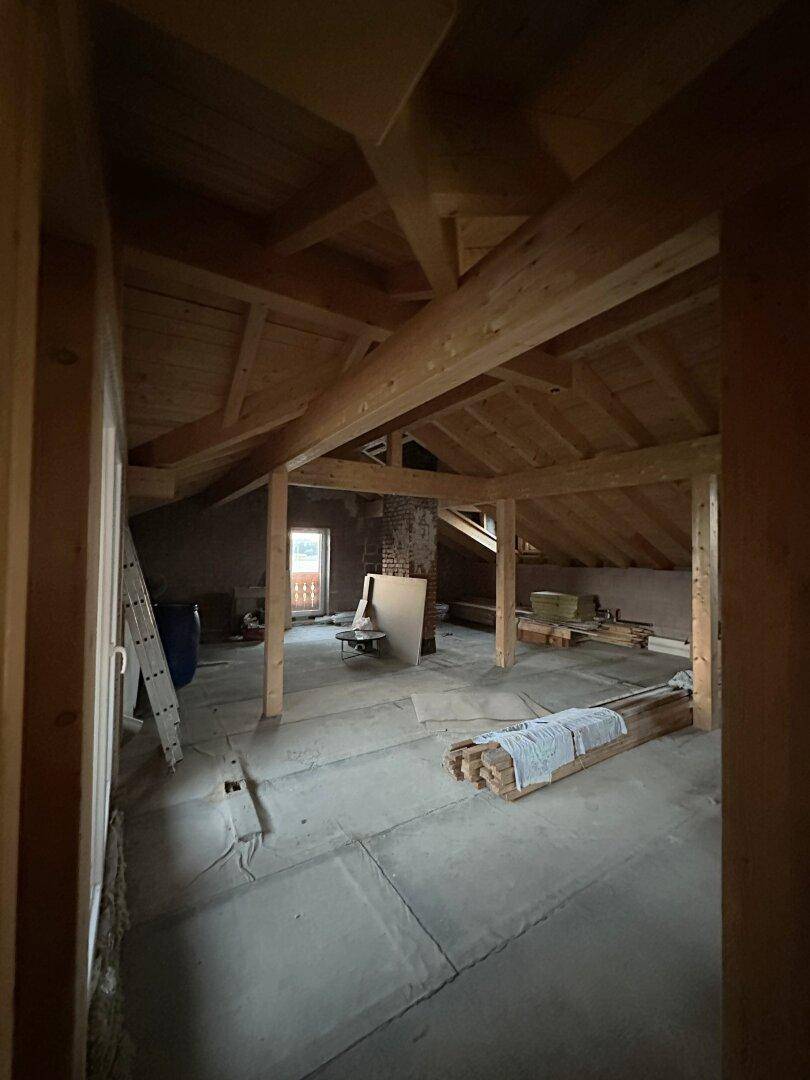 Unfertiger Dachboden mit sichtbaren Holzbalken und viel Potenzial für zukünftigen Ausbau.