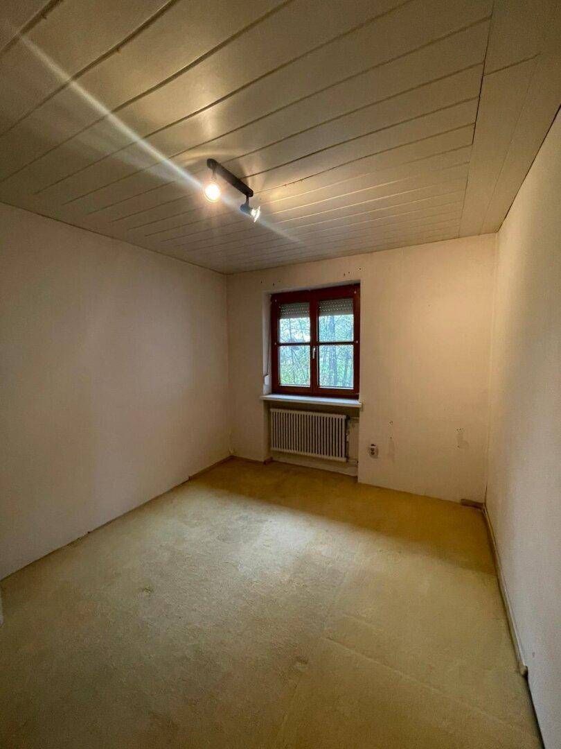 Schlafzimmer mit gelbem Teppichboden, einem Fenster und einfacher Deckenverkleidung, bereit zur Renovierung.