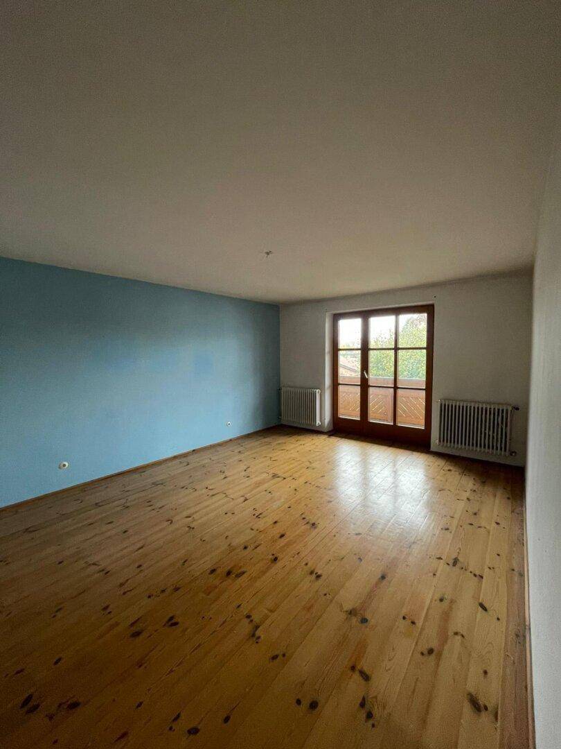 Heller Raum mit Dielenboden, einer blauen Akzentwand und Zugang zu einem Balkon durch eine Glastür.