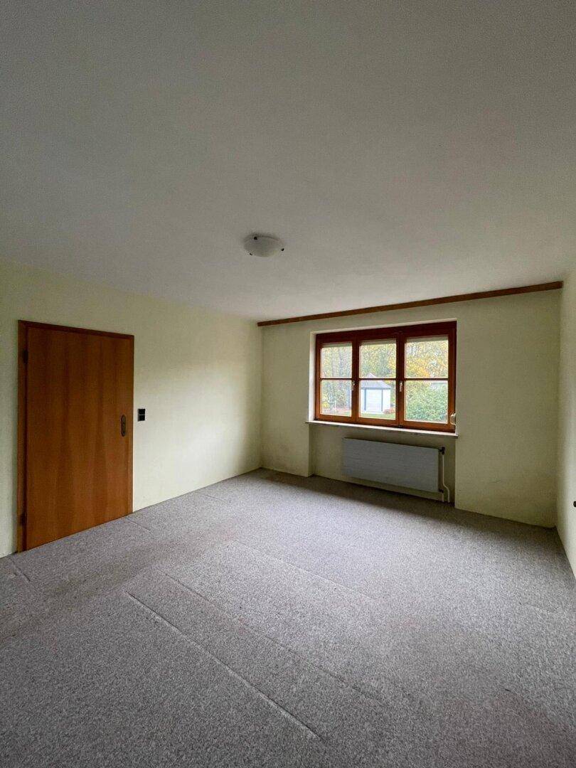 Schlafzimmer mit grauem Teppichboden, einem Fenster und einer Holztür, ideal für individuelle Gestaltung.