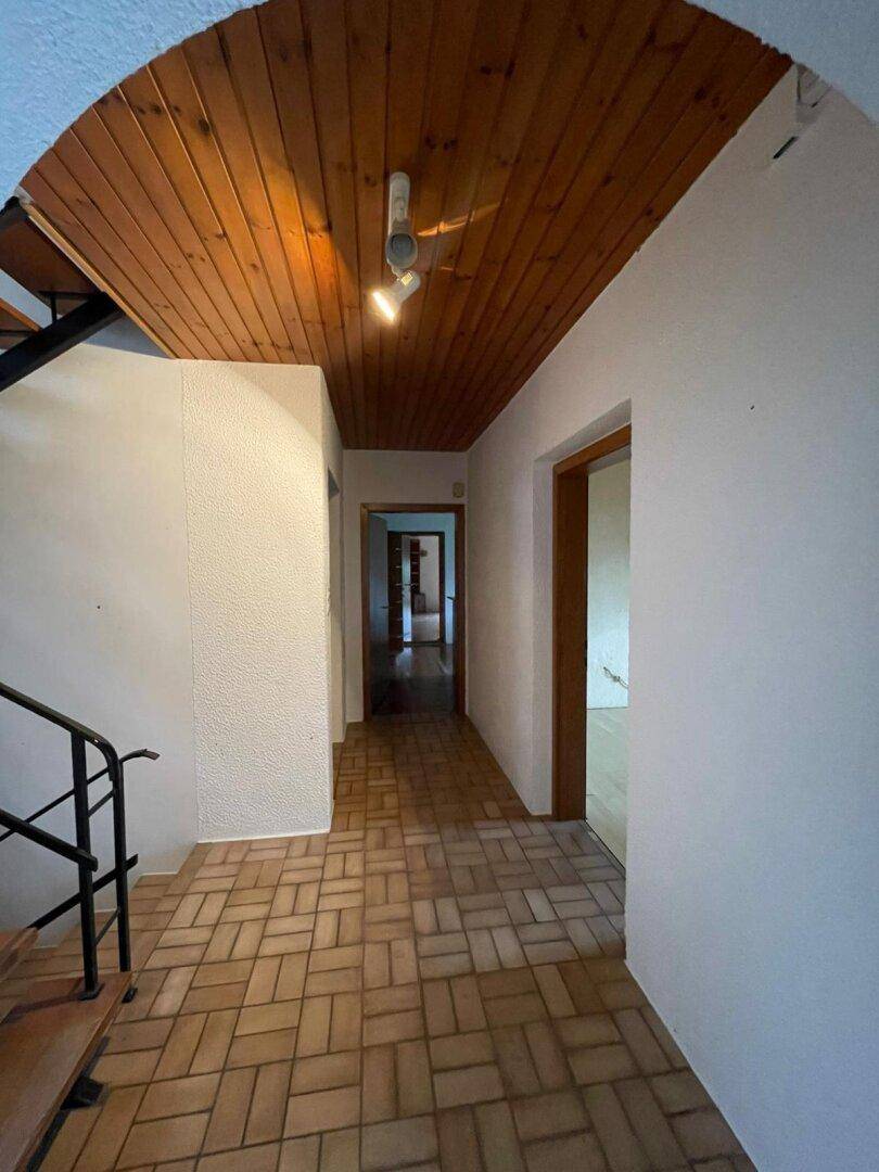 Flur mit Fliesenboden, Holzdecke und einem Bogen, der zum Treppenhaus führt, in traditionellem Stil.