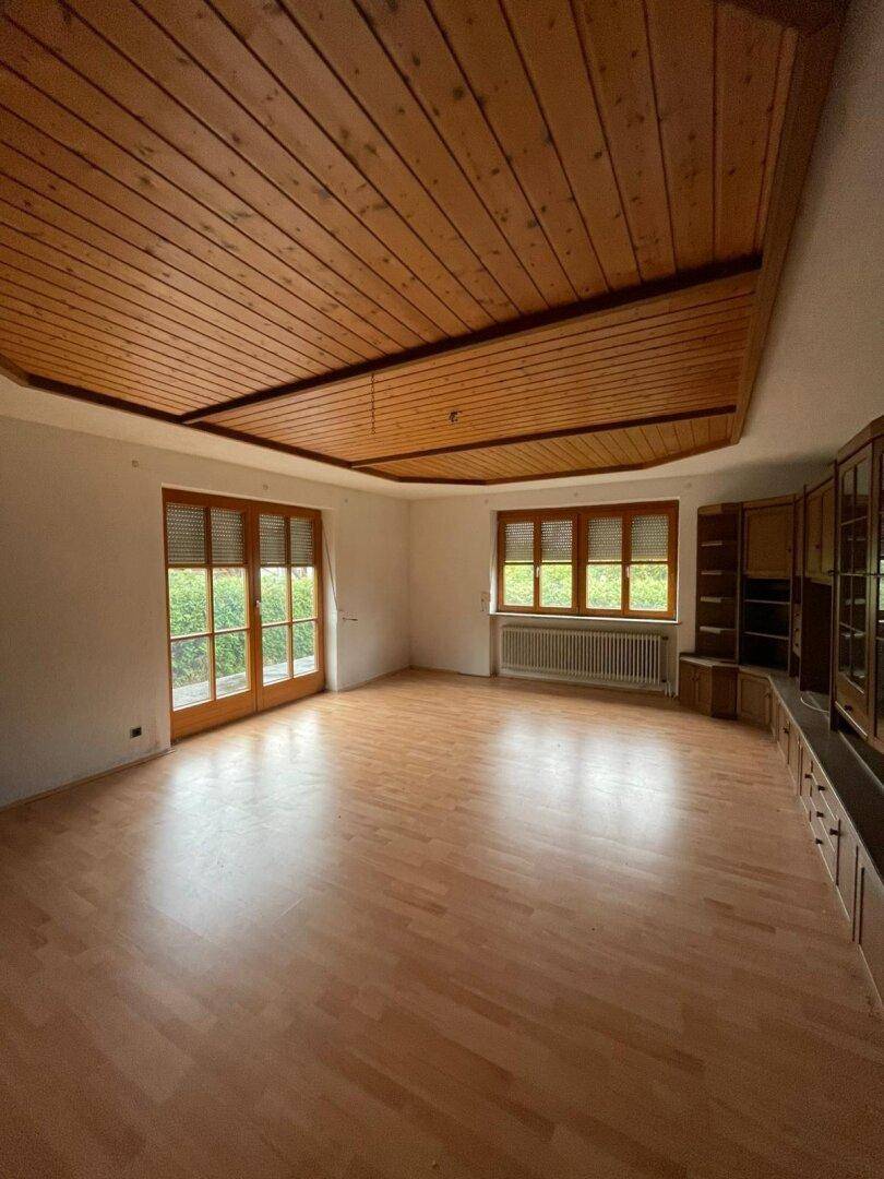 Geräumiges Wohnzimmer mit Holzlaminatboden, Holzdecke und großen Fenstern, die viel Licht hereinlassen.