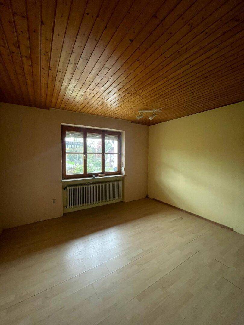 Schlafzimmer mit Holzlaminatboden, Holzdecke und einem Fenster, das Tageslicht hereinlässt.