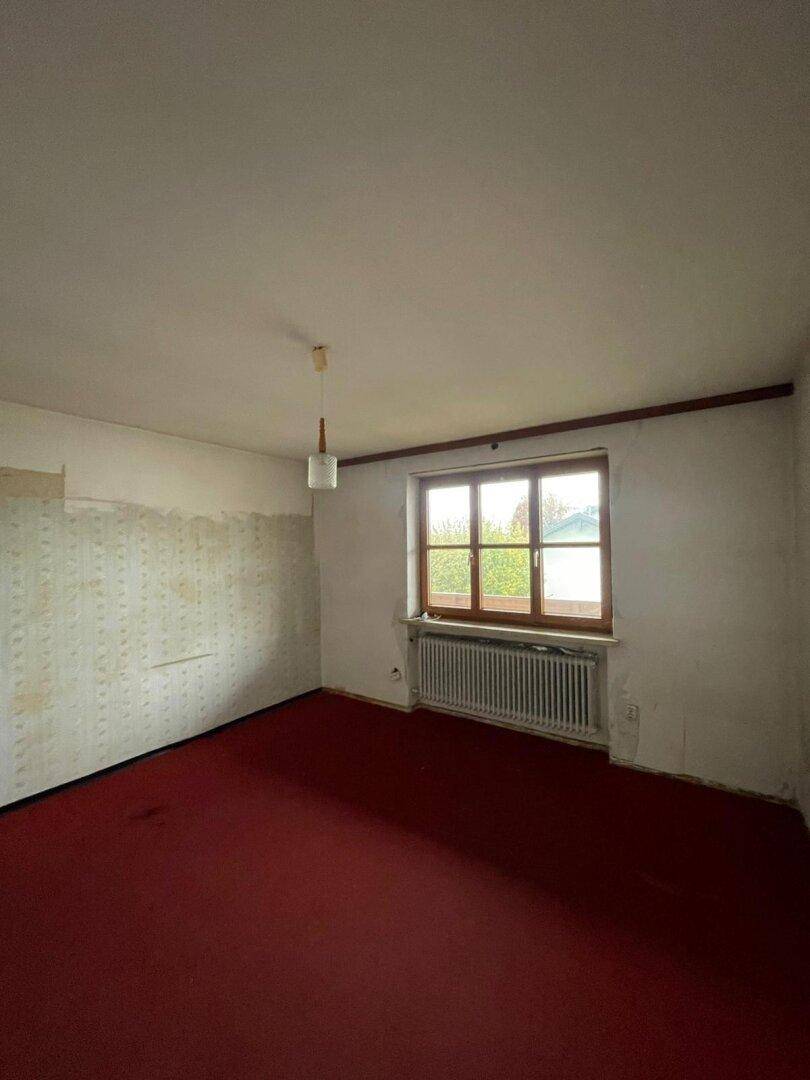 Schlafzimmer mit rotem Teppichboden und einem Fenster, das auf eine Renovierung wartet.