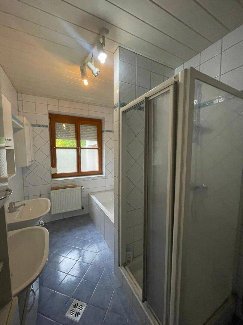 Badezimmer mit blauen Fliesen, Badewanne, Duschkabine, Doppelwaschbecken und einem Fenster.