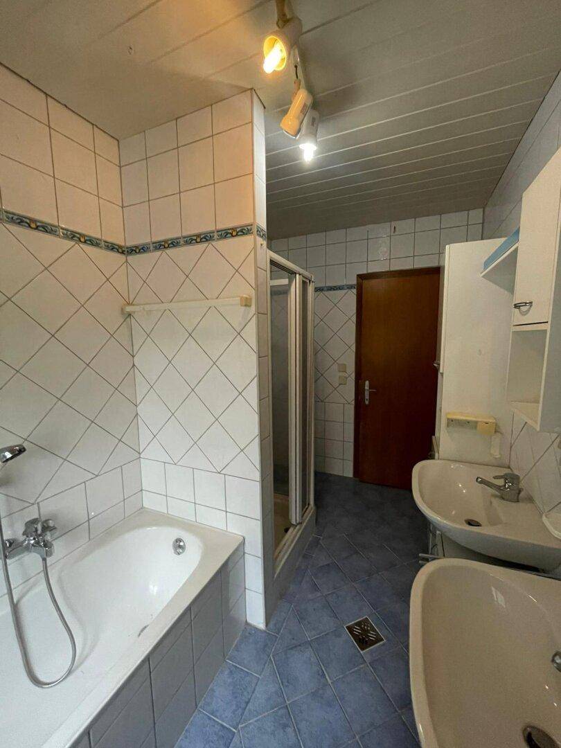 Badezimmer mit blauen Fliesen, Badewanne und Duschkabine, ausgestattet mit zwei Waschbecken.