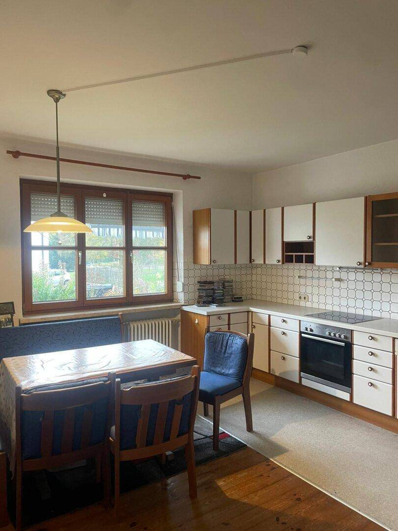 Helle Küche mit Essbereich, weißen Schränken, Fliesenrückwand und Blick ins Grüne durch das Fenster.