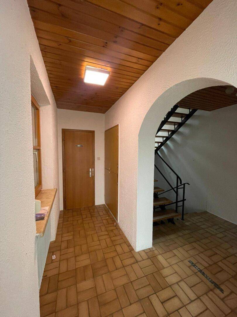 Eingangsbereich mit Fliesenboden, Holzdecke und einem Bogen, der zum Treppenhaus führt.