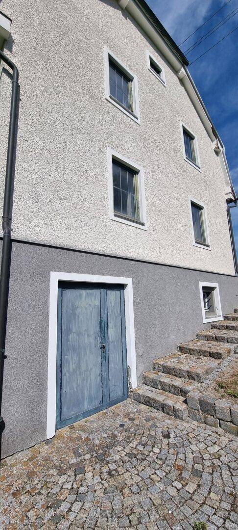 Seitenansicht des Gebäudes mit Kellerzugang und Steintreppe auf Kopfsteinpflaster.