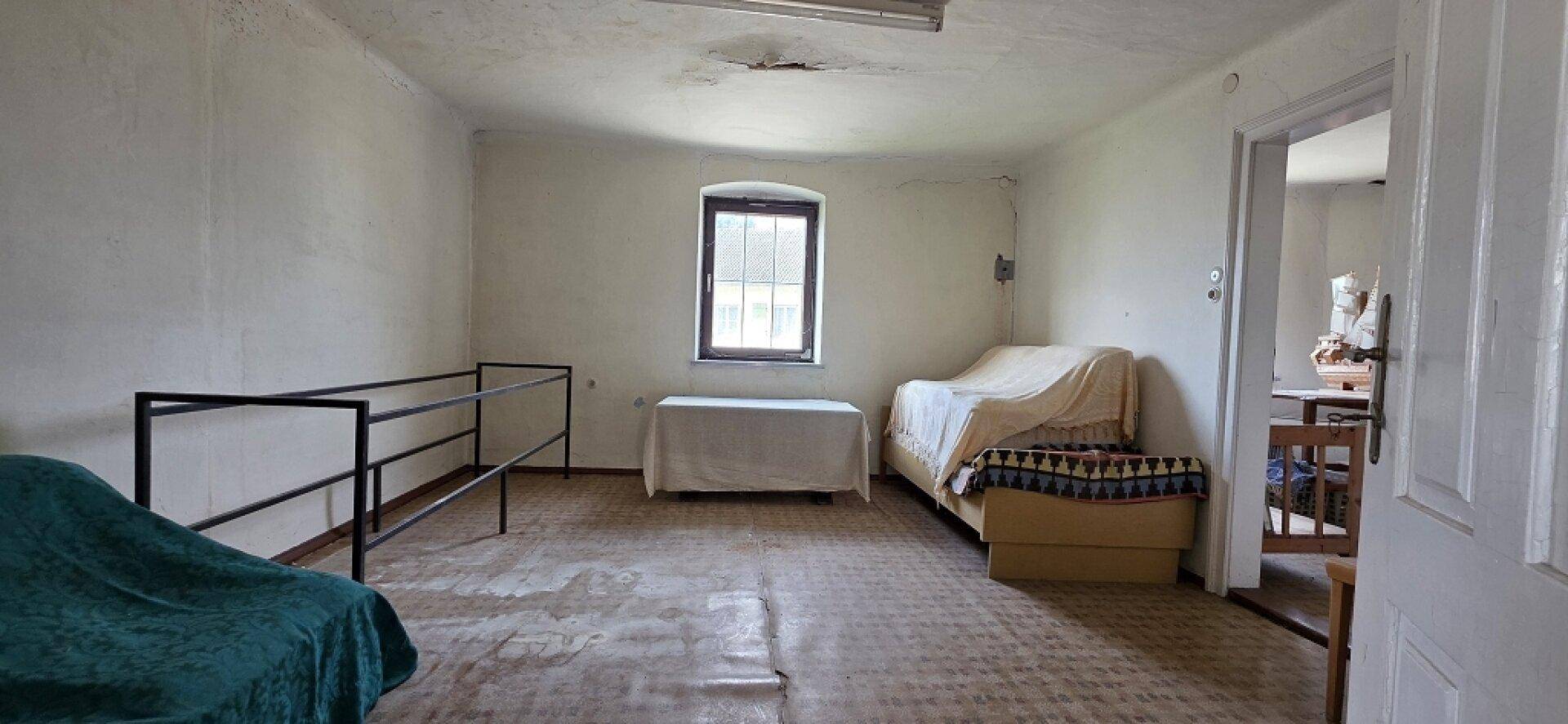 Einfaches Zimmer mit Fenster, zwei Betten und sichtbaren Abnutzungserscheinungen.