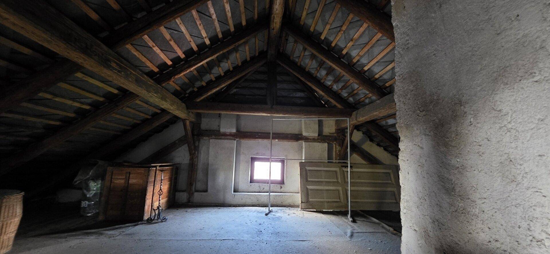 Dachboden mit freiliegenden Holzbalken, kleinem Fenster und viel Potenzial für Ausbau.