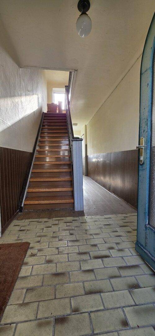 Eingangsbereich mit gefliestem Boden, Holztreppe und Holztäfelung an den Wänden.