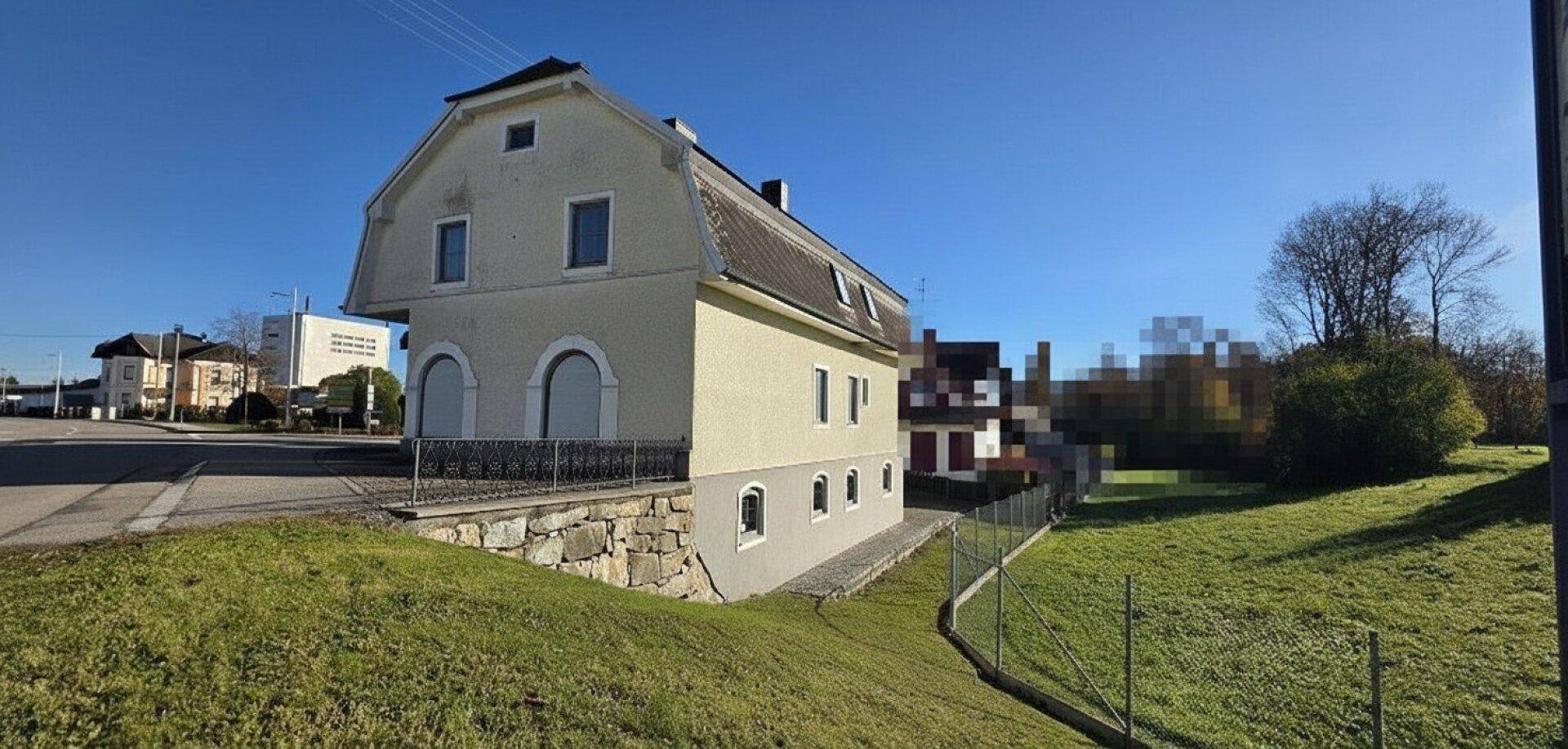 Seitenansicht des Gebäudes mit Hanglage, Steinmauer und weitem Blick ins Grüne.