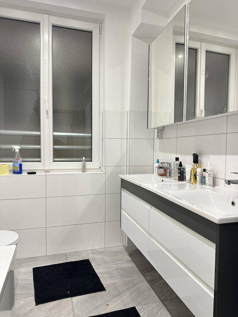 Helles Badezimmer mit Doppelwaschbecken, Spiegelschrank und großem Fenster.