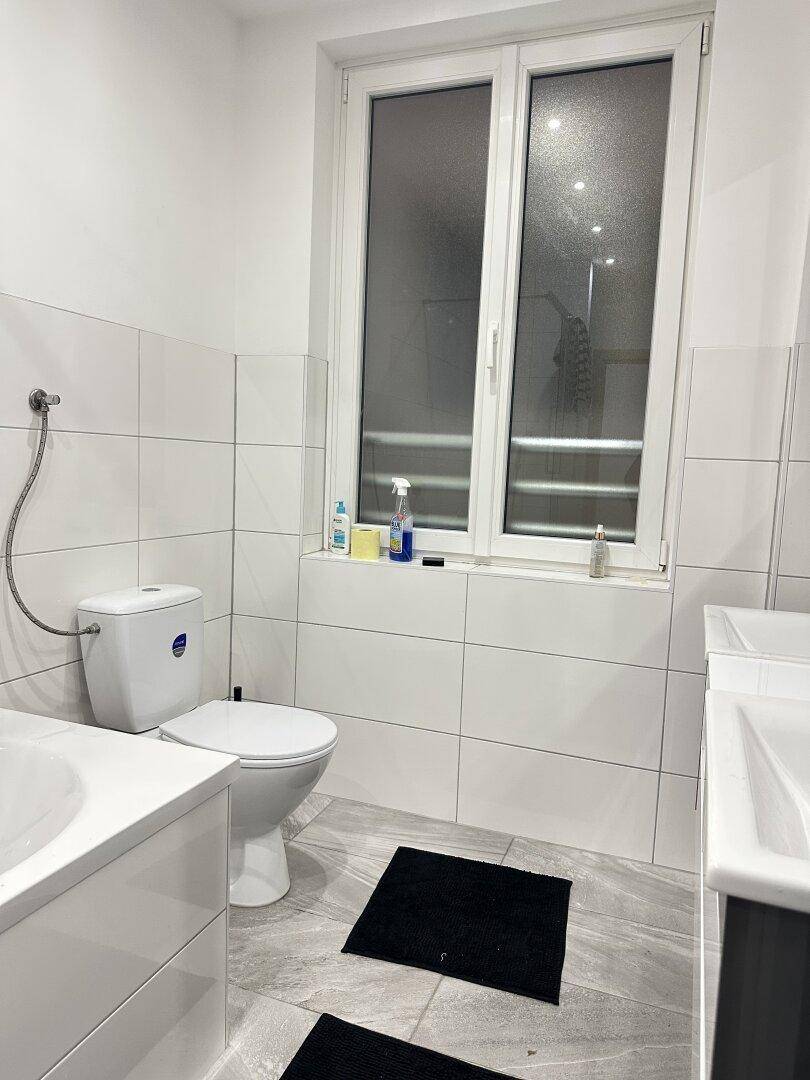 Badezimmer mit Toilette, Fenster und modernen Fliesen, gut beleuchtet.
