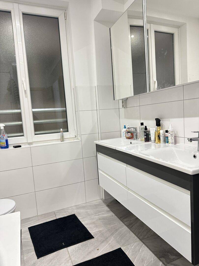 Modernes Badezimmer mit Doppelwaschbecken, Spiegelschrank und großem Fenster.