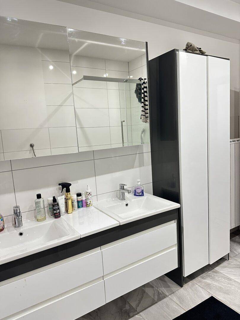 Badezimmer mit Doppelwaschbecken, Spiegelschrank und hohem weißen Schrank.