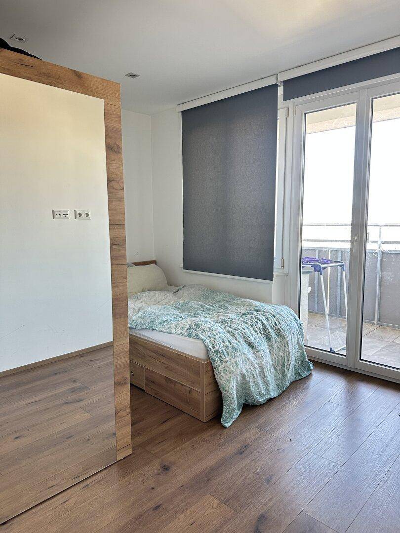 Schlafzimmer mit Holzbett, Parkettboden und Zugang zu einem Balkon.