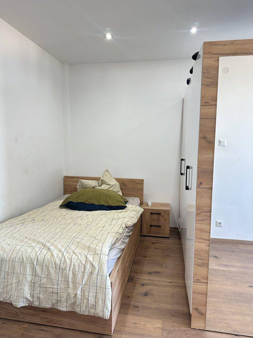 Helles Schlafzimmer mit Holzbett, Nachttisch und Parkettboden.