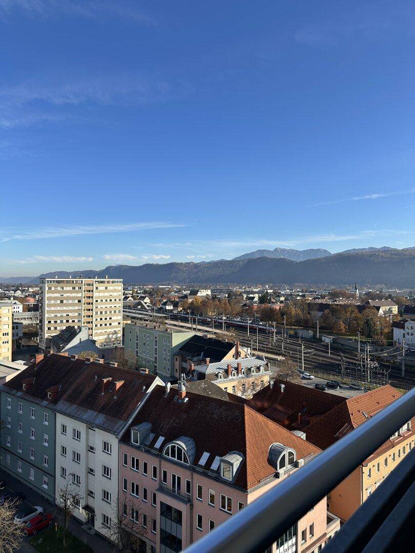 Weitläufiger Blick über die Stadt mit Bahngleisen und Bergen im Hintergrund.
