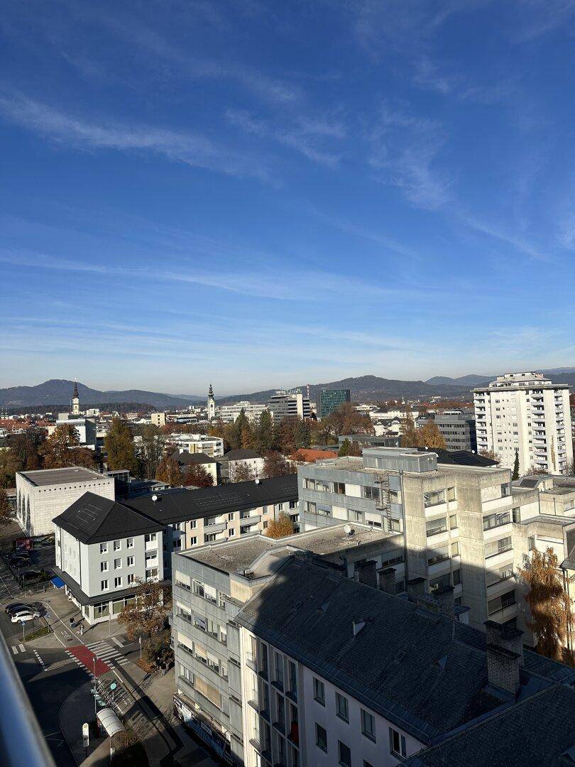 Weitläufiger Blick über die Stadt mit Bergen im Hintergrund unter blauem Himmel.