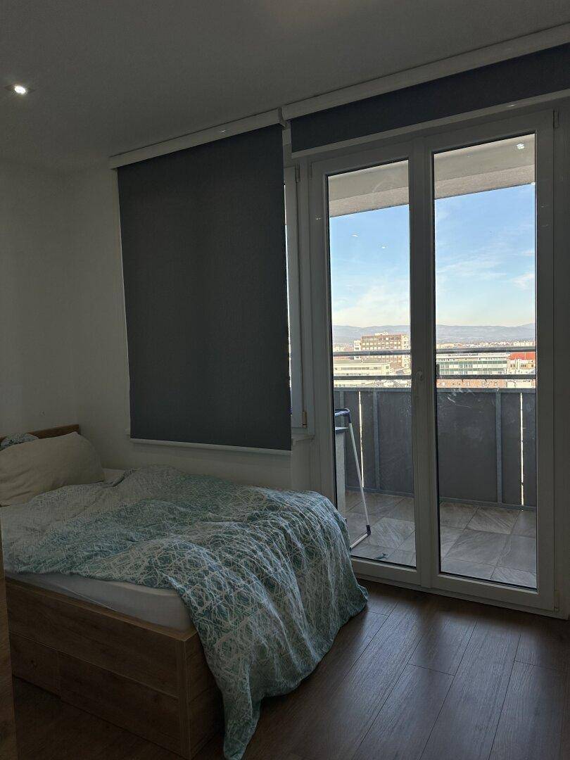 Schlafzimmer mit Holzbett, Parkettboden und Balkonzugang mit Blick ins Freie.