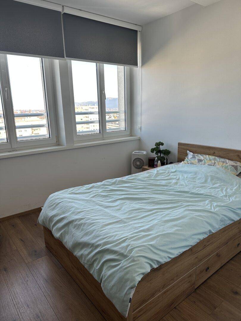 Schlafzimmer mit Holzbett, Parkettboden und großen Fenstern mit Stadtblick.