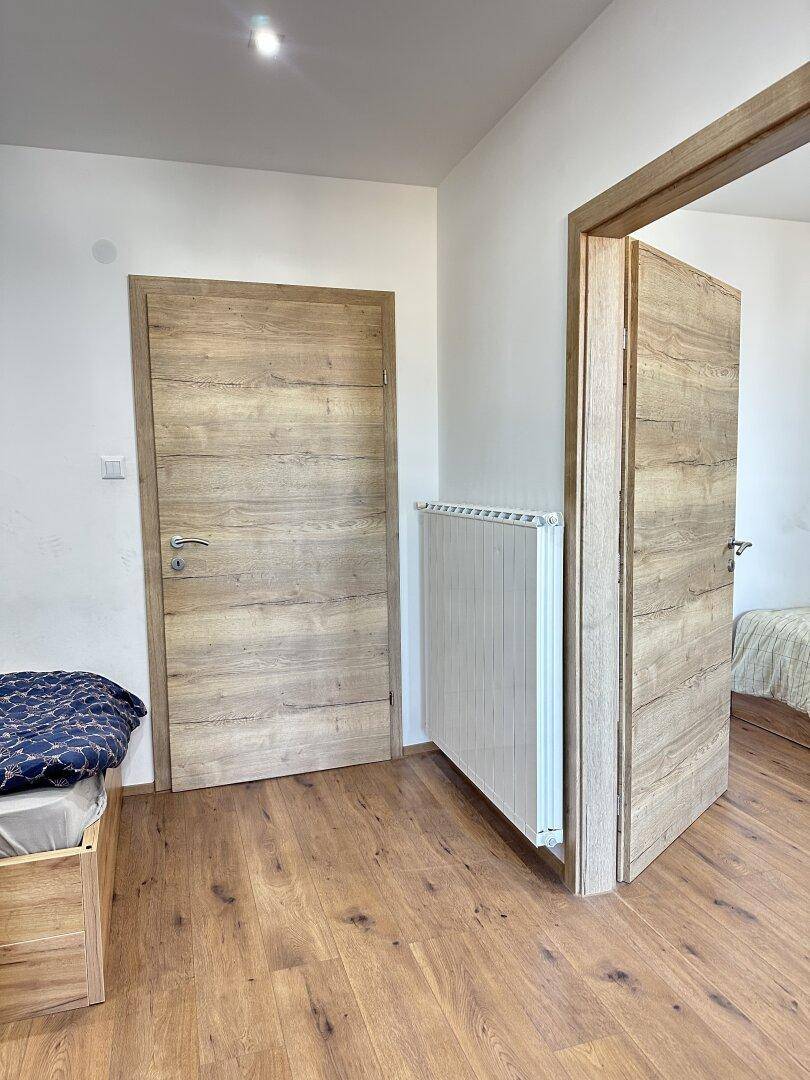 Schlafzimmer mit Holzboden, Heizkörper und zwei Holztüren, die zu anderen Räumen führen.