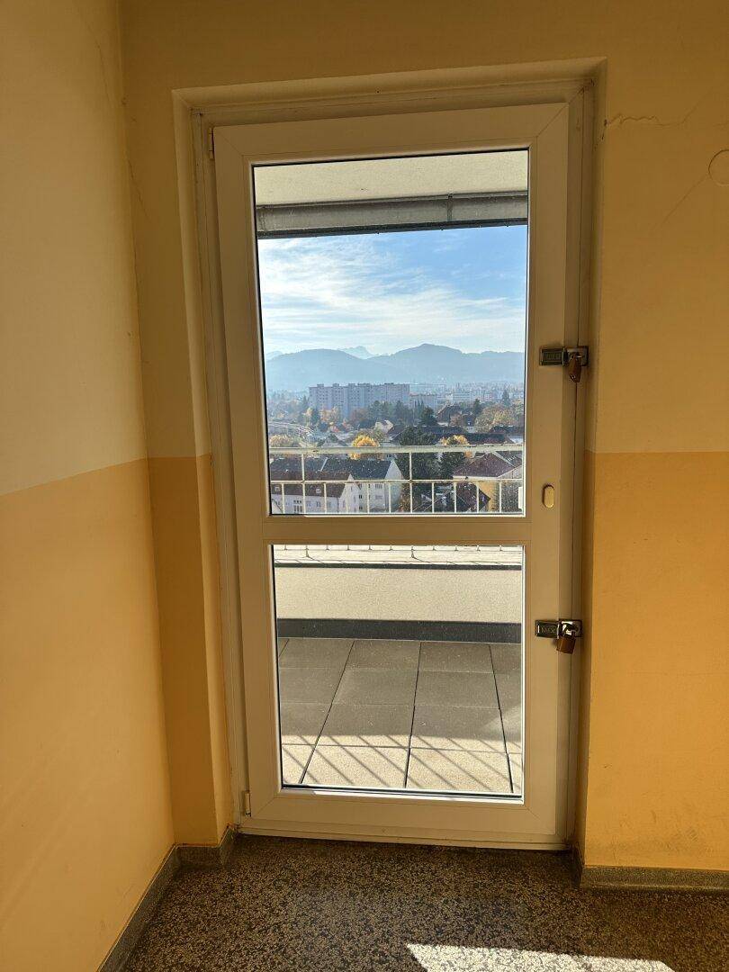 Heller Flur mit einer Tür, die zu einem Außenbereich mit Stadt- und Bergblick führt.