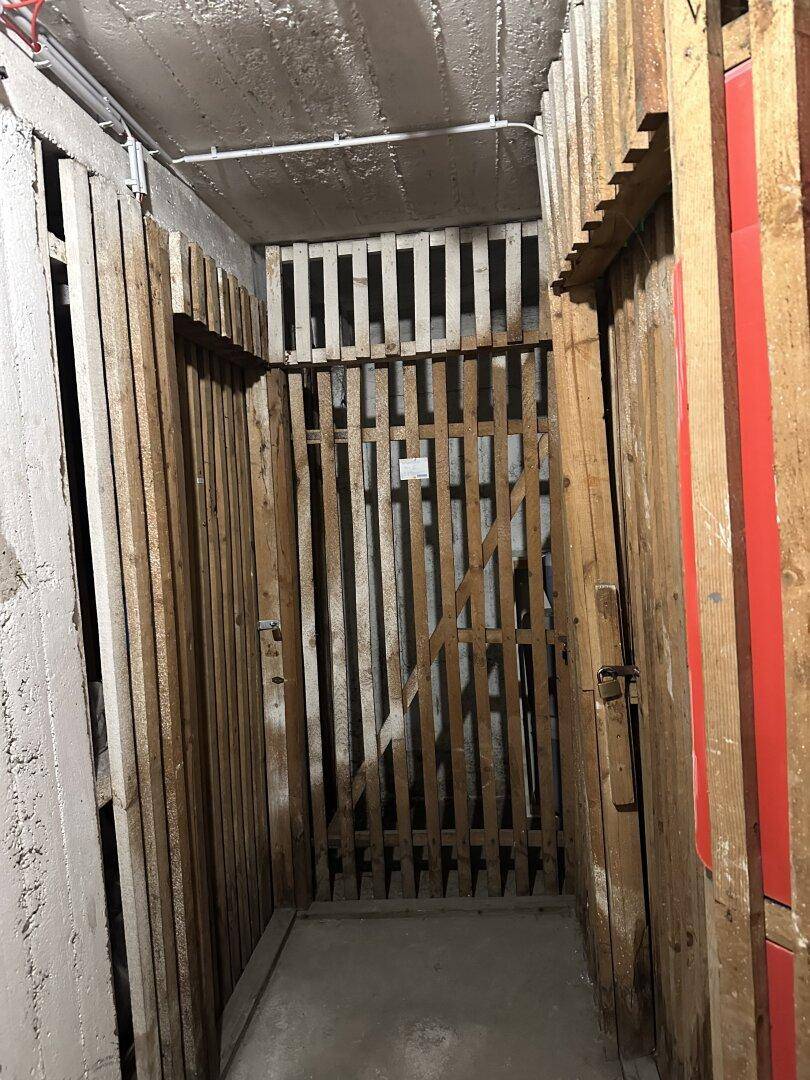 Einfacher Lagerraum mit Holzlattenwänden und Betonboden im Kellerbereich.